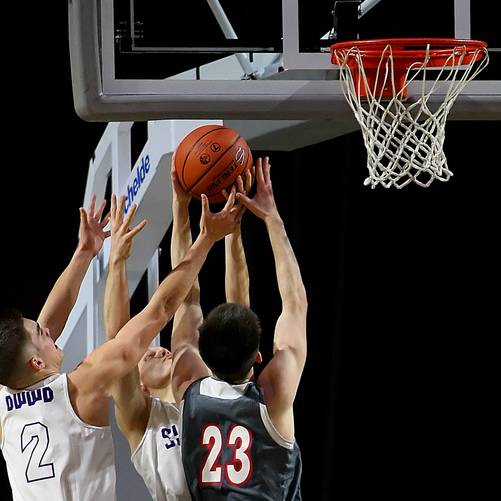 Six hands go after one basketball near the basket.