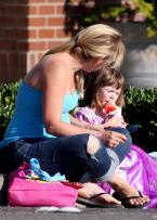 Trying to stay cool, a young girl enjoys a snow cone as mom has a lollipop.