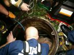 A rescue worker reaches down to lift up the white and tan dog out of a sewer manhol