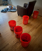 A child sleeps on the floor amid buckets collecting drips from the leaking roof. Photo by Patrick Robinson